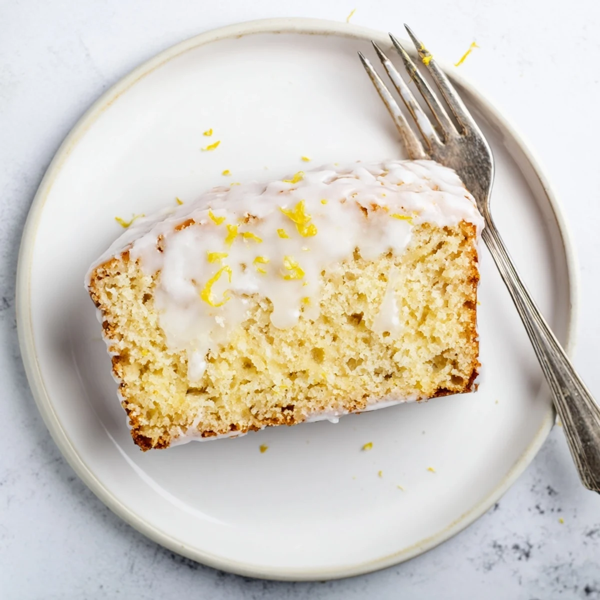 Fresh Greek yogurt lemon loaf with lemon glaze and whole lemon slices on marble surface
