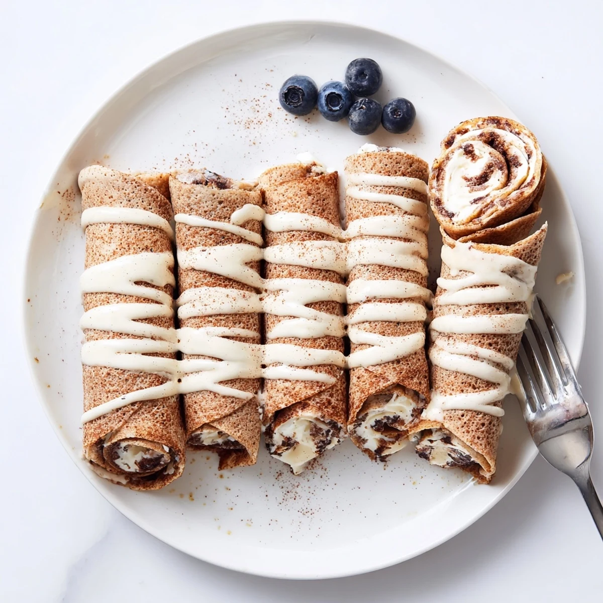 Warm Cinnamon Roll Protein Crepes rolled with creamy cinnamon filling and glaze