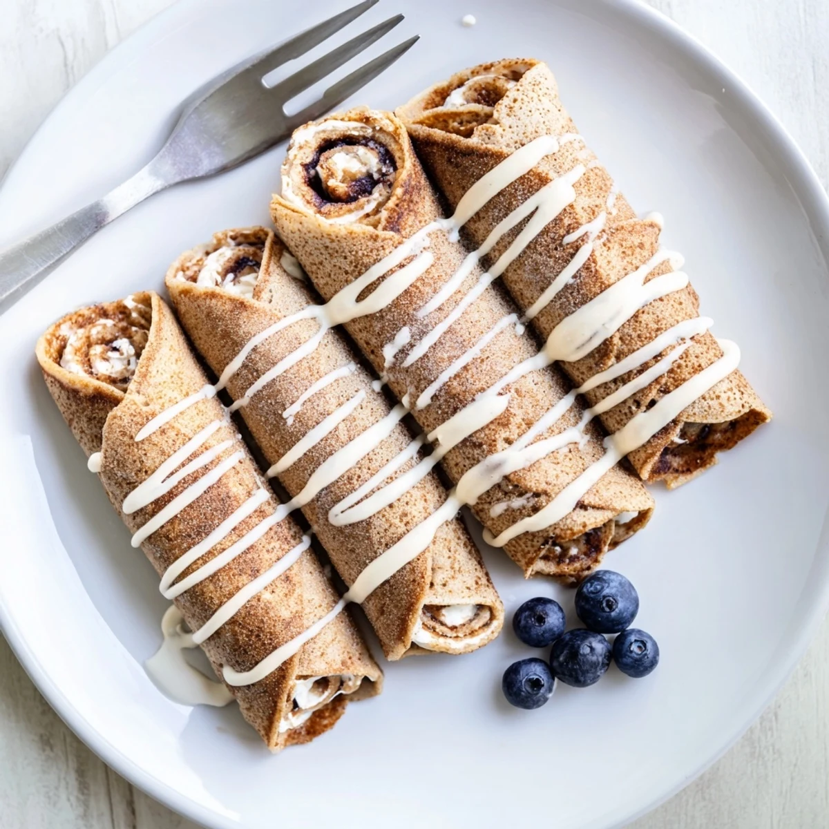 Stacked Cinnamon Roll Protein Crepes topped with light glaze and aromatic cinnamon