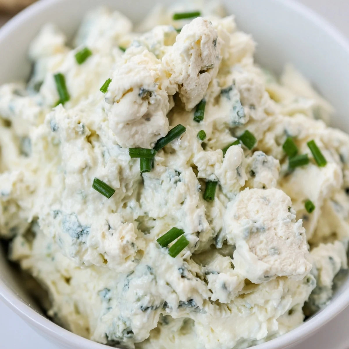 Thick blue cheese dip topped with chopped chives in a rustic serving bowl