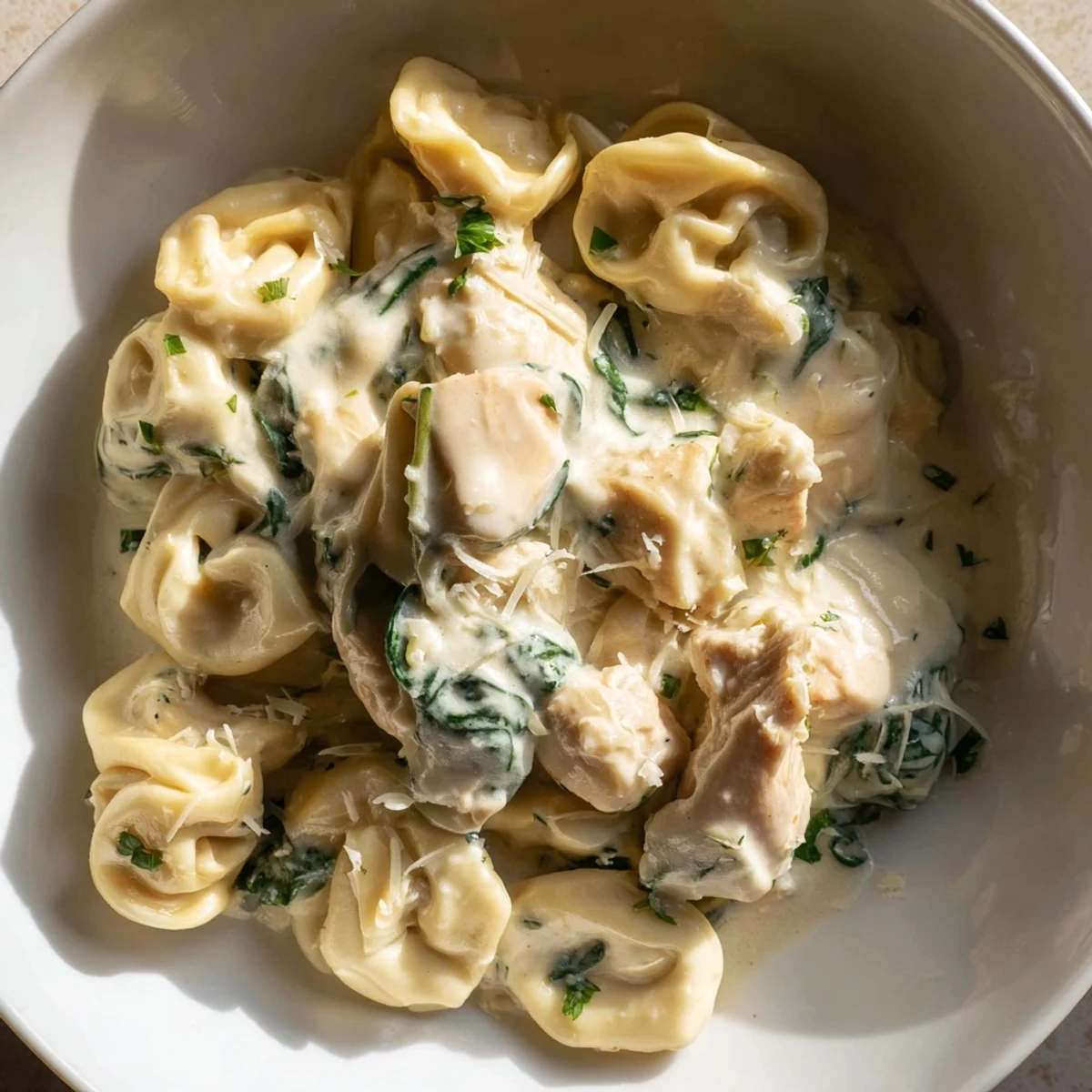 Steaming bowl of creamy garlic chicken tortellini with wilted spinach and Parmesan garnish