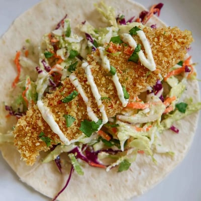 Golden-brown Crispy Fish Tacos with Cabbage Slaw served on a wooden board, topped with vibrant purple cabbage slaw and fresh cilantro leaves.