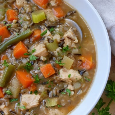 Hearty Chicken Vegetable Soup with Wild Rice ladled into a rustic bowl, showcasing chunks of chicken, celery, and green beans in savory broth.