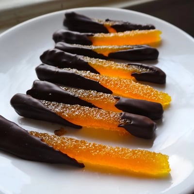 Candied orange peel strips dipped halfway in smooth melted dark chocolate, cooling on wire rack